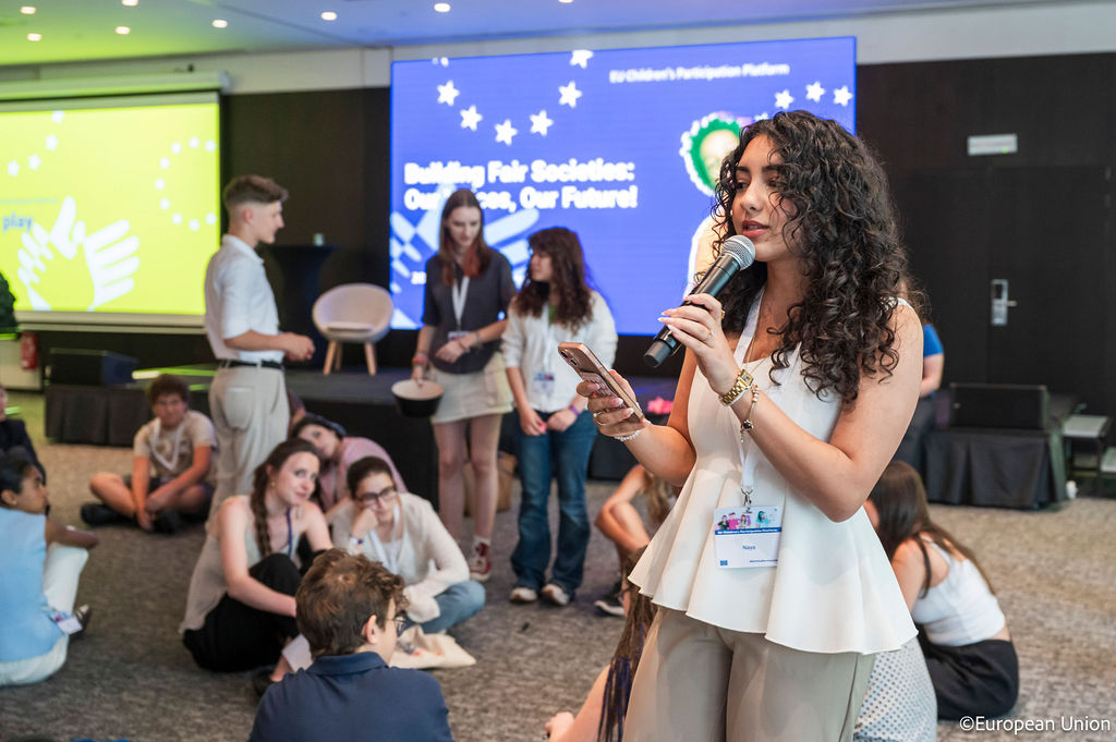 A teenage girl making announcements to a room full of young participants