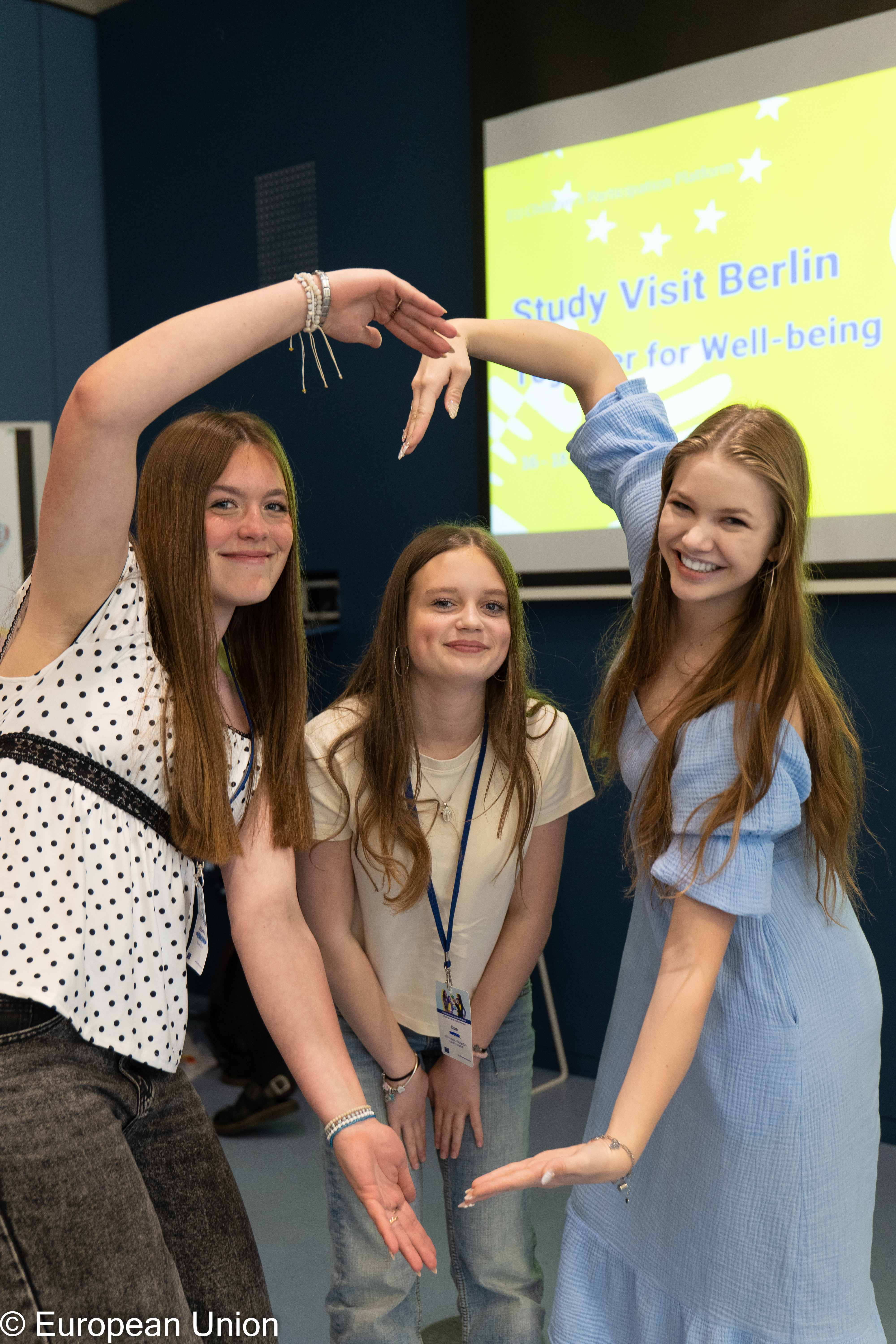 Three teenage girls smiling at the camera and forming a heart shape with hands.