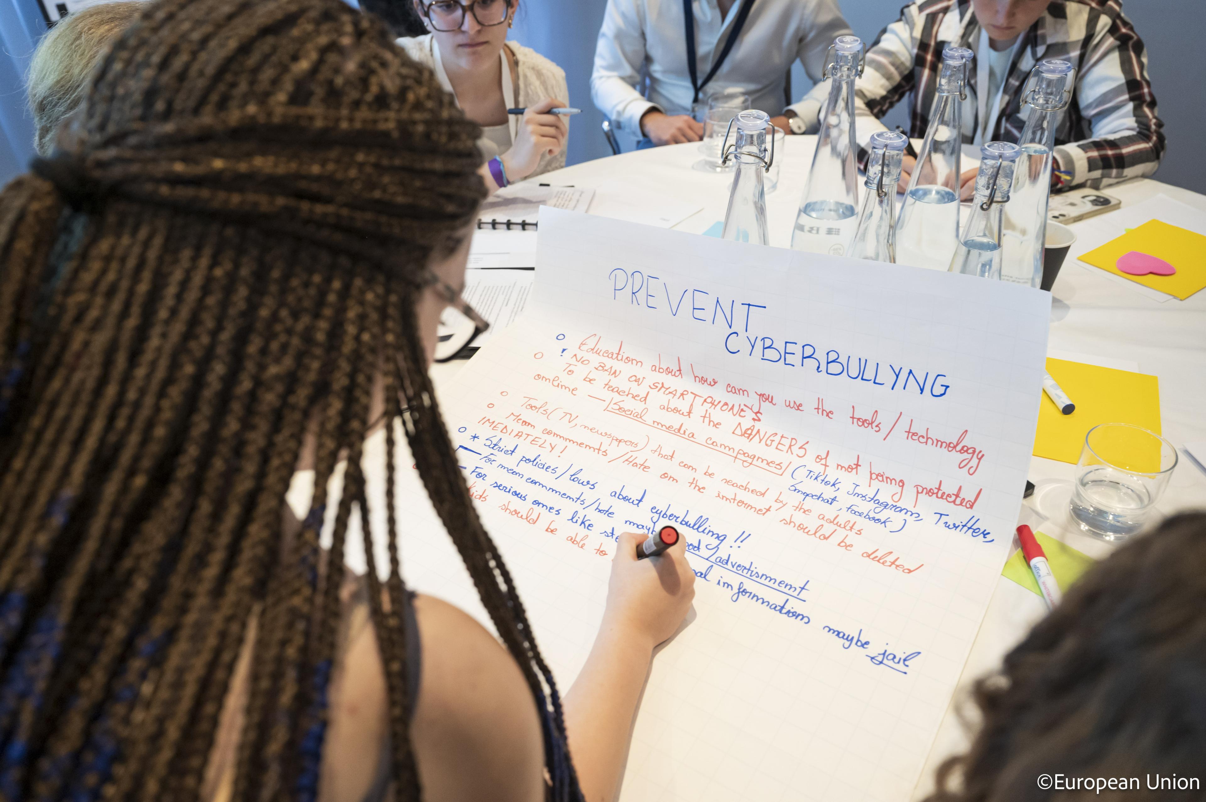 A young person writing “Prevent Cyberbullying” on a large sheet during a workshop session at the General Assembly meeting in 2025.