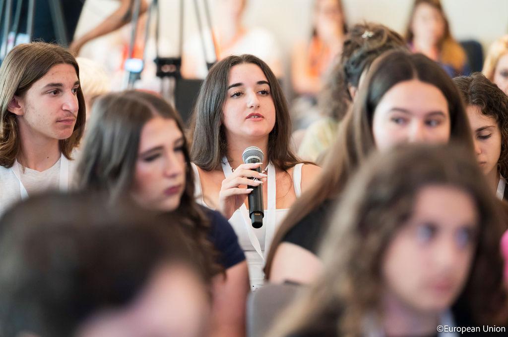 A girl speaking into a microphone during a large meeting