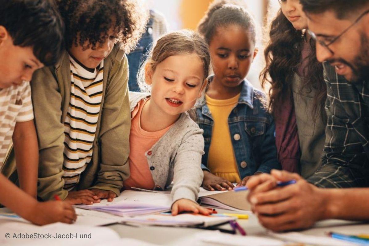 A group of kids working around desk together with their teacher.