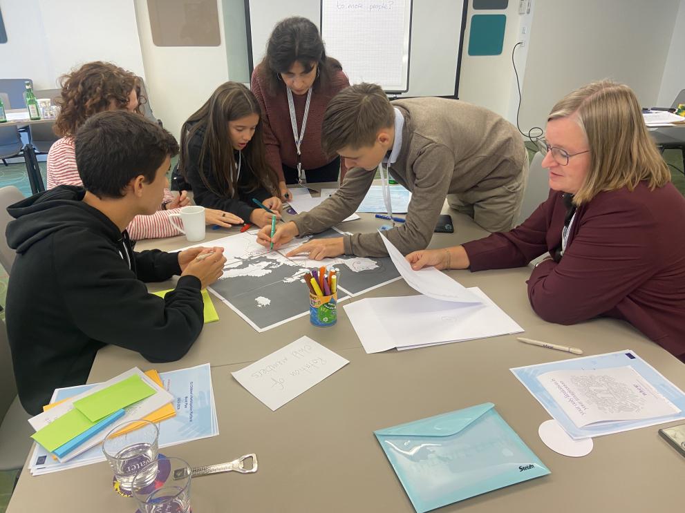 A group of children and adults working together on a project at a table in a meeting room. 