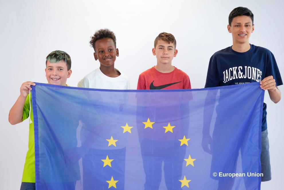 A group of four boys of different ages holding a big EU flag