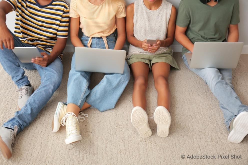 Four teens sitting on the floor with computers on their laps