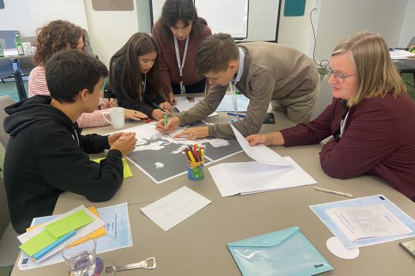 A group of children and adults working together on a project at a table in a meeting room. 